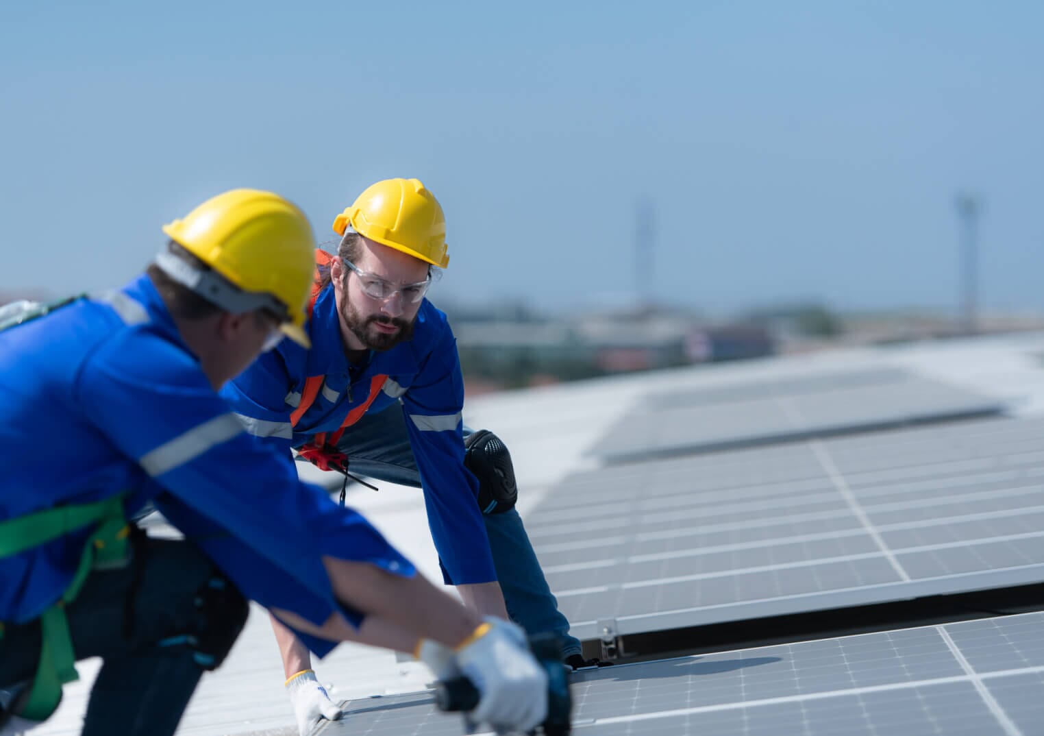 Two workmen in hard hats installing a solar panel, looking at each other