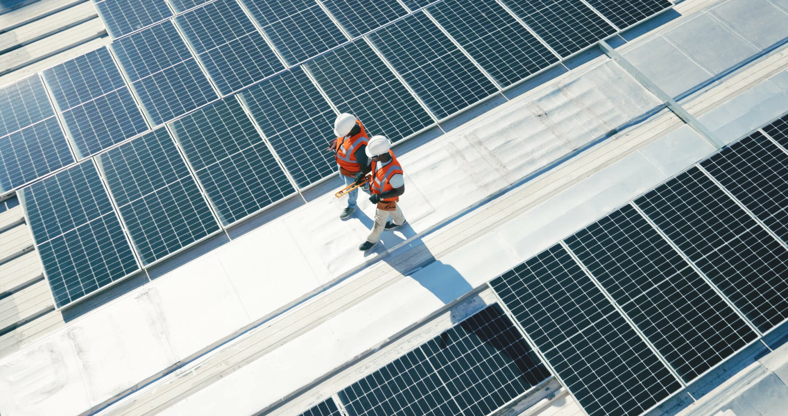 Two men in high-vis walking on a roof with solar panels installed